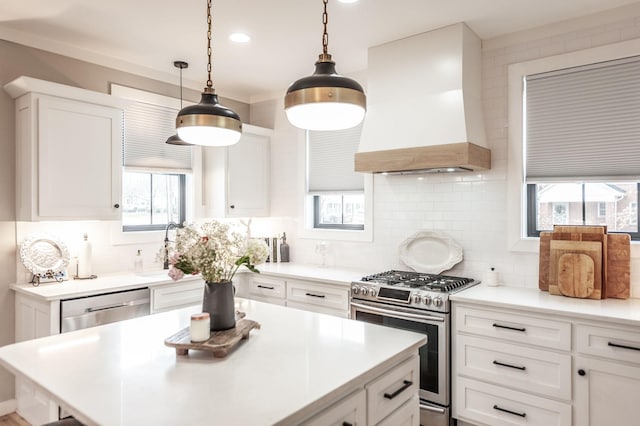 kitchen with custom exhaust hood, white cabinetry, hanging light fixtures, stainless steel appliances, and decorative backsplash