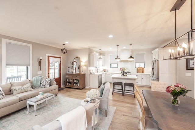 living room featuring an inviting chandelier, ornamental molding, sink, and light hardwood / wood-style flooring