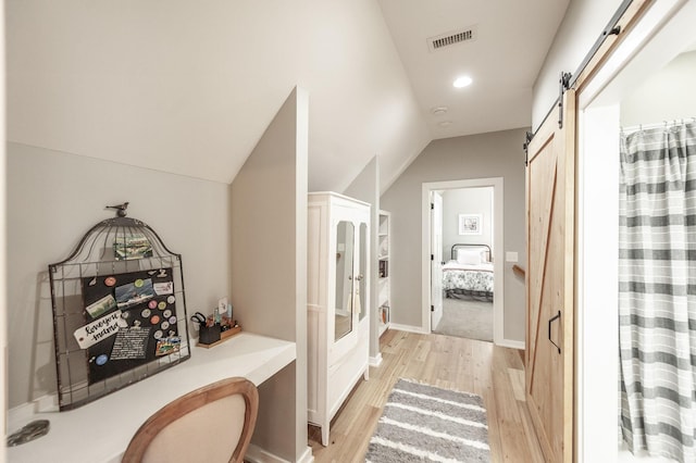 hall with light hardwood / wood-style flooring, a barn door, and vaulted ceiling