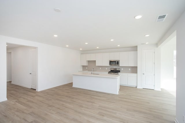 kitchen featuring decorative backsplash, appliances with stainless steel finishes, a center island with sink, and white cabinets