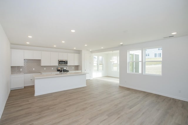 kitchen with appliances with stainless steel finishes, an island with sink, white cabinets, backsplash, and light hardwood / wood-style floors