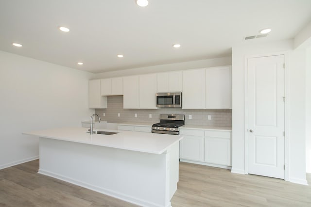 kitchen with sink, appliances with stainless steel finishes, a kitchen island with sink, decorative backsplash, and white cabinets