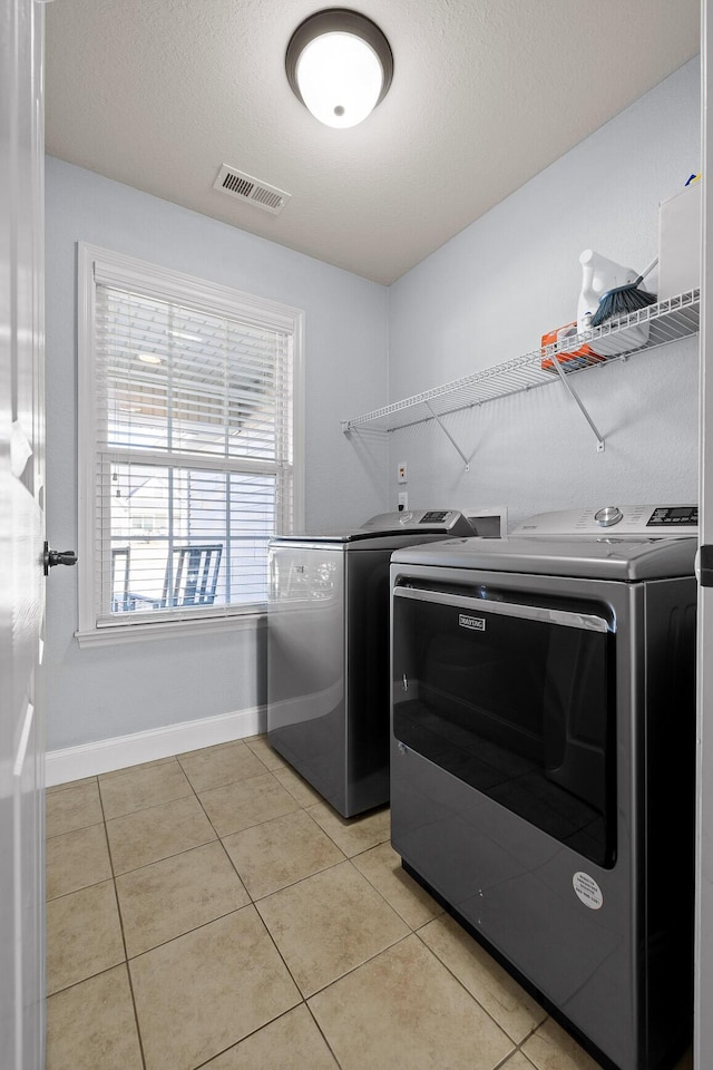 washroom featuring light tile patterned floors, a textured ceiling, and washer and clothes dryer