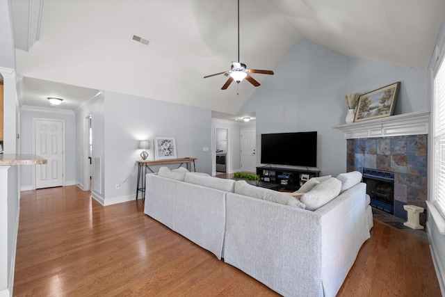 living room featuring crown molding, wood-type flooring, high vaulted ceiling, a tile fireplace, and ceiling fan