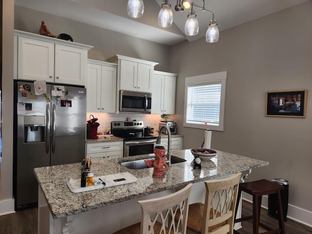 kitchen with white cabinetry, appliances with stainless steel finishes, a kitchen island with sink, and decorative light fixtures