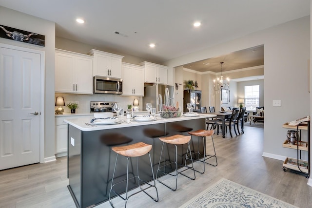 kitchen featuring stainless steel appliances, a kitchen island with sink, white cabinets, and a breakfast bar