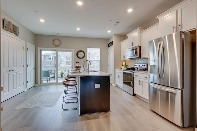 kitchen with stainless steel appliances, sink, a kitchen island with sink, and white cabinets