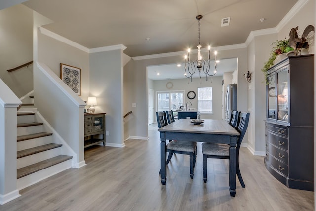 dining space featuring a notable chandelier, ornamental molding, and light wood-type flooring