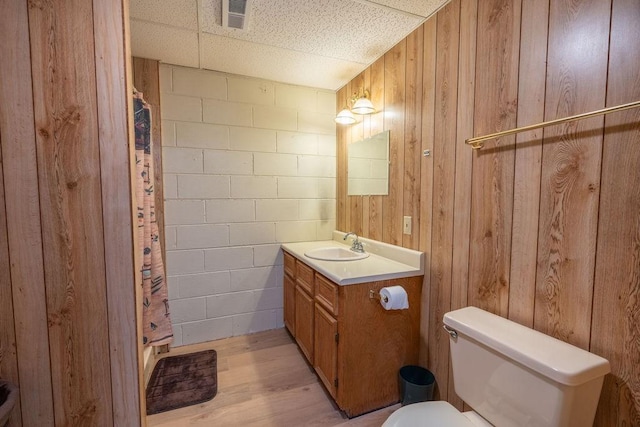 bathroom with wooden walls, hardwood / wood-style flooring, vanity, walk in shower, and toilet