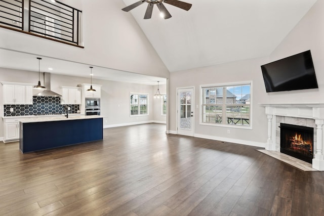 unfurnished living room with dark wood-type flooring, ceiling fan, a fireplace, and high vaulted ceiling