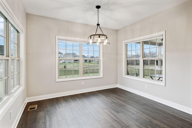 unfurnished dining area with plenty of natural light, a notable chandelier, and dark hardwood / wood-style flooring