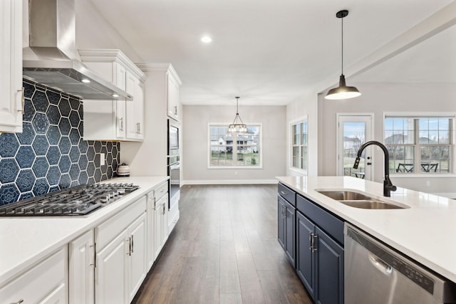 kitchen featuring appliances with stainless steel finishes, decorative light fixtures, sink, white cabinets, and wall chimney range hood