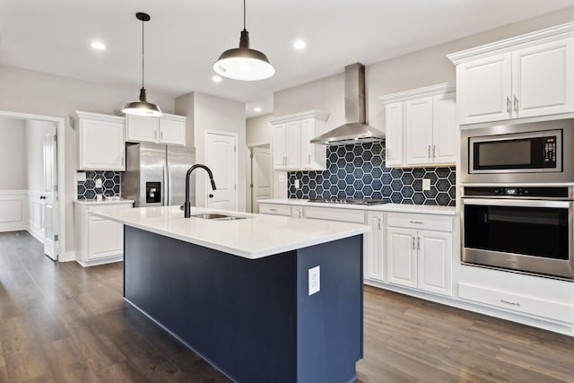 kitchen featuring wall chimney exhaust hood, sink, white cabinetry, a center island with sink, and appliances with stainless steel finishes