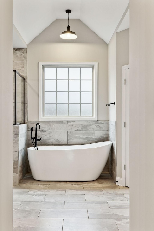 bathroom featuring tile walls, a bathtub, and vaulted ceiling