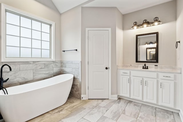 bathroom featuring vanity, vaulted ceiling, tile walls, and a washtub