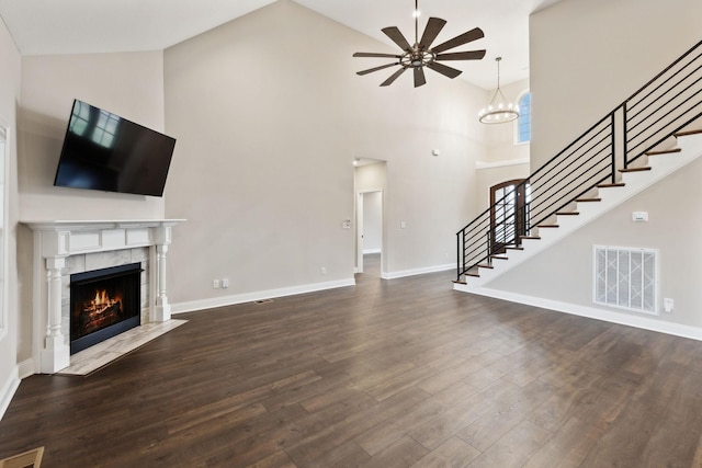 unfurnished living room featuring a towering ceiling, a tile fireplace, dark hardwood / wood-style floors, and ceiling fan