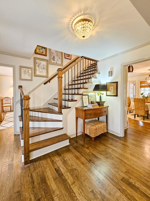 stairs featuring wood-type flooring, ornamental molding, and a chandelier