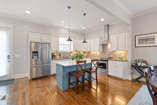 kitchen featuring white cabinets, appliances with stainless steel finishes, decorative light fixtures, and wall chimney range hood