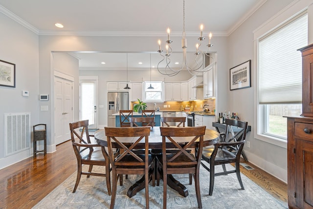 dining room with hardwood / wood-style flooring, ornamental molding, plenty of natural light, and an inviting chandelier