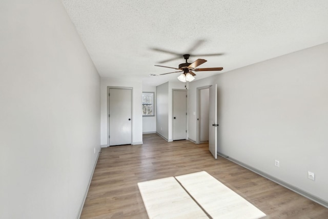 unfurnished bedroom featuring ceiling fan, light hardwood / wood-style floors, a textured ceiling, and two closets