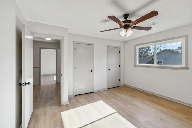 unfurnished bedroom with ceiling fan, two closets, a textured ceiling, and light wood-type flooring