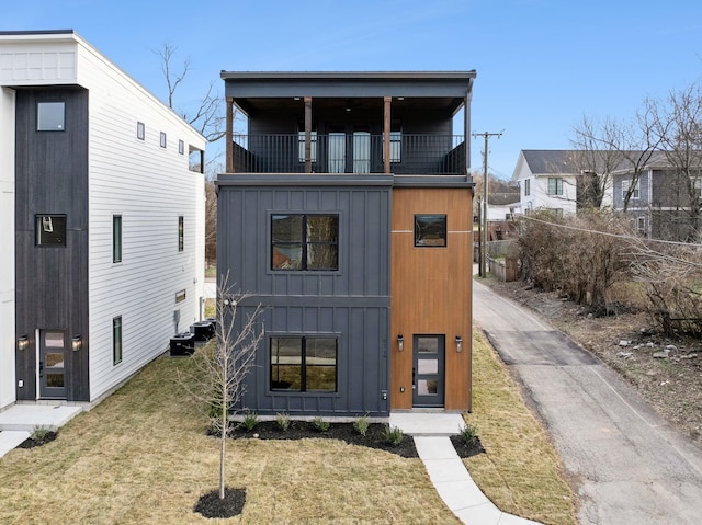 view of front of home with a balcony, central AC, and a front lawn