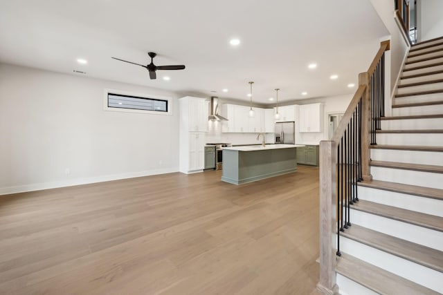 kitchen featuring appliances with stainless steel finishes, hanging light fixtures, an island with sink, white cabinets, and wall chimney exhaust hood