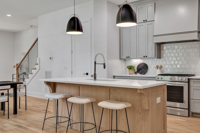 kitchen with decorative light fixtures, a kitchen island with sink, gas stove, and gray cabinetry