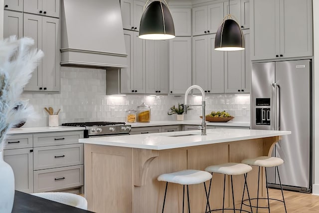 kitchen featuring sink, premium range hood, a kitchen island with sink, hanging light fixtures, and stainless steel appliances