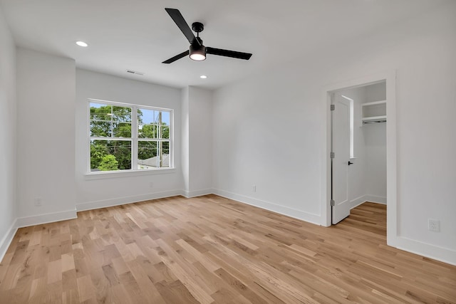 unfurnished bedroom featuring ceiling fan, a walk in closet, and light hardwood / wood-style floors