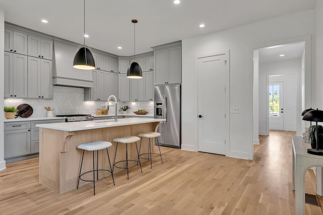 kitchen featuring a breakfast bar, an island with sink, sink, stainless steel appliances, and custom range hood