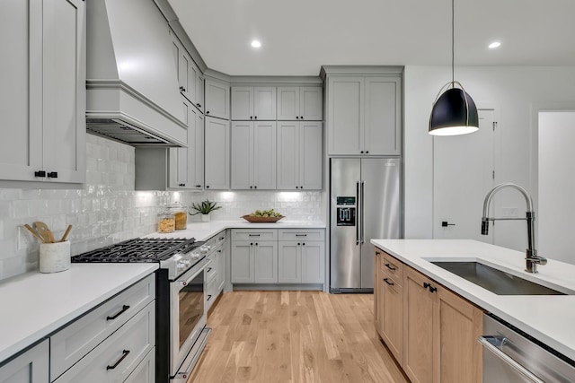 kitchen with pendant lighting, sink, backsplash, stainless steel appliances, and light wood-type flooring