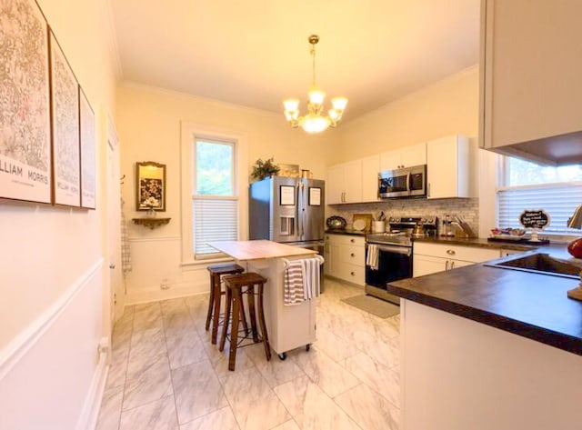 kitchen featuring sink, white cabinetry, crown molding, decorative light fixtures, and appliances with stainless steel finishes