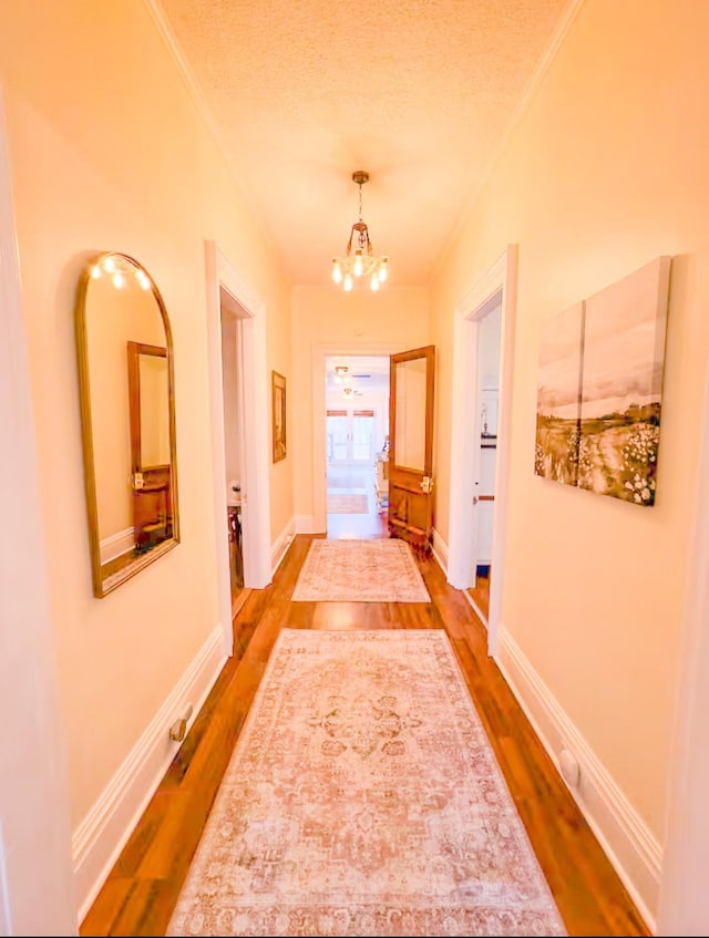 hall featuring a notable chandelier, hardwood / wood-style flooring, ornamental molding, and a textured ceiling