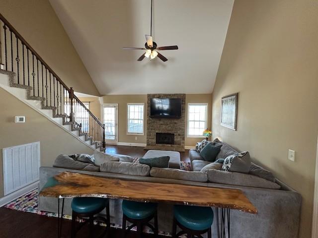 living room with high vaulted ceiling, a stone fireplace, wood finished floors, visible vents, and stairway