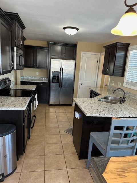 kitchen with light tile patterned floors, light stone counters, stainless steel appliances, a sink, and pendant lighting