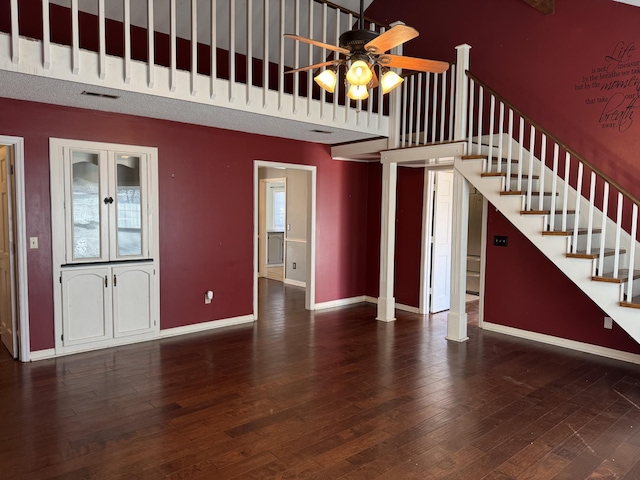 unfurnished living room with dark wood-type flooring, ceiling fan, decorative columns, and a high ceiling