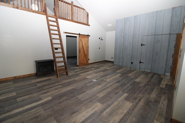 unfurnished living room featuring a barn door, dark wood-type flooring, and high vaulted ceiling