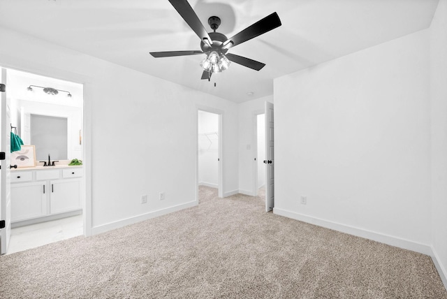 unfurnished bedroom featuring connected bathroom, sink, a spacious closet, light colored carpet, and ceiling fan