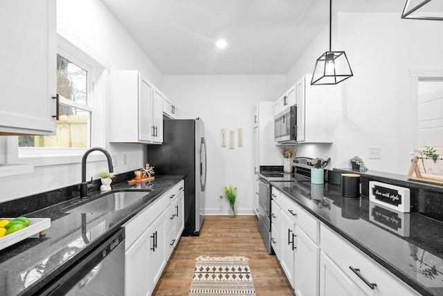 kitchen with stainless steel appliances, hanging light fixtures, sink, and dark stone countertops