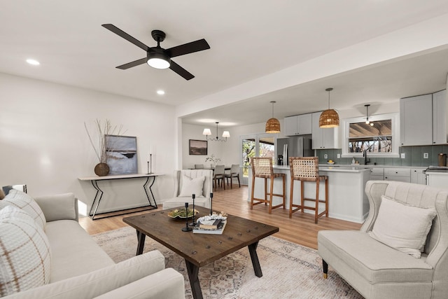 living room with ceiling fan with notable chandelier and light hardwood / wood-style flooring