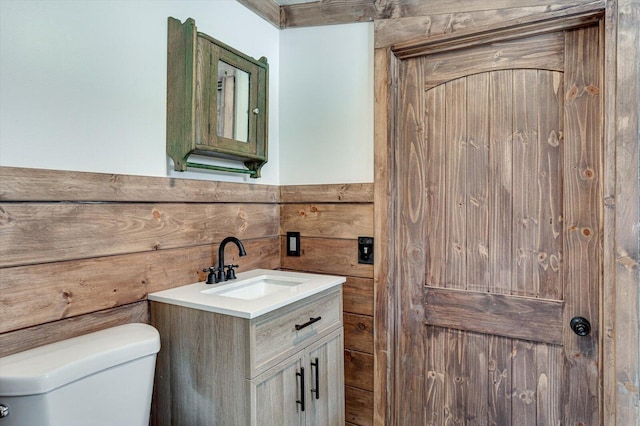 half bath with wainscoting, vanity, toilet, and wooden walls