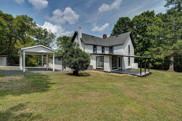 rear view of property with a lawn, a chimney, gravel driveway, a patio area, and a carport