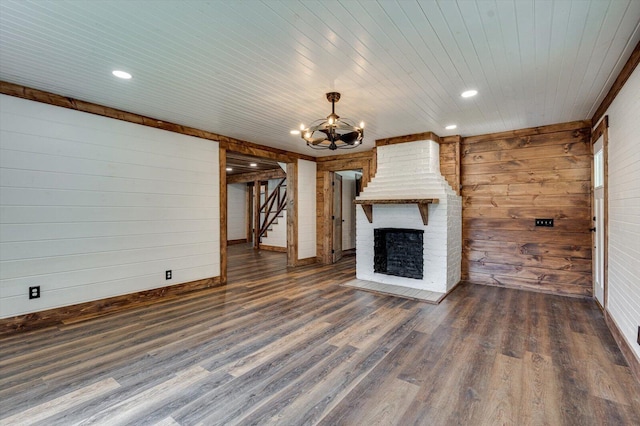 unfurnished living room with a chandelier, wood walls, stairway, a brick fireplace, and dark wood-style floors