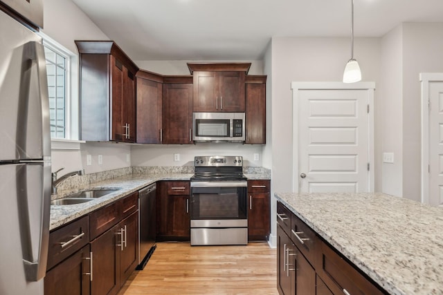 kitchen featuring pendant lighting, sink, appliances with stainless steel finishes, light hardwood / wood-style floors, and light stone countertops