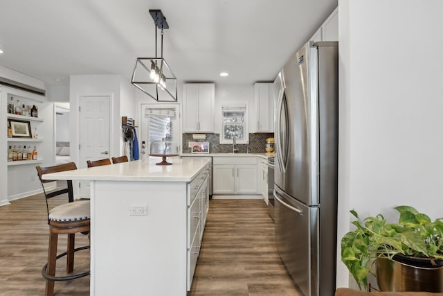 kitchen with pendant lighting, stainless steel refrigerator, white cabinetry, a center island, and a kitchen bar