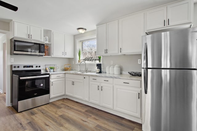 kitchen with white cabinetry, light stone countertops, sink, wood-type flooring, and appliances with stainless steel finishes