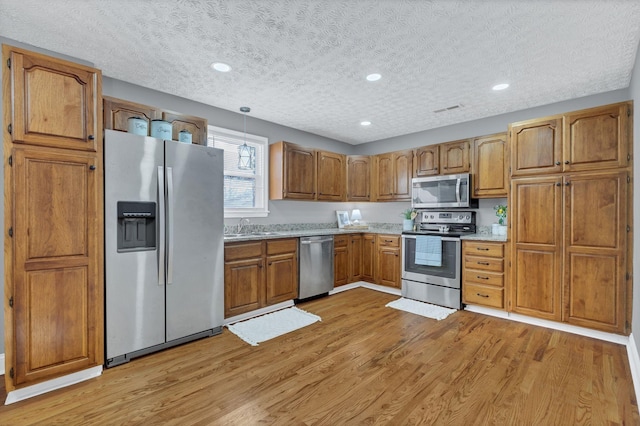 kitchen with sink, hanging light fixtures, stainless steel appliances, a textured ceiling, and light wood-type flooring