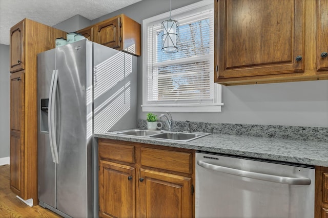 kitchen featuring sink, decorative light fixtures, a textured ceiling, light hardwood / wood-style flooring, and appliances with stainless steel finishes