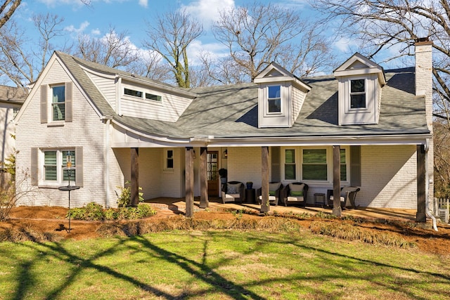 view of front of property with a porch, brick siding, roof with shingles, a front lawn, and a chimney